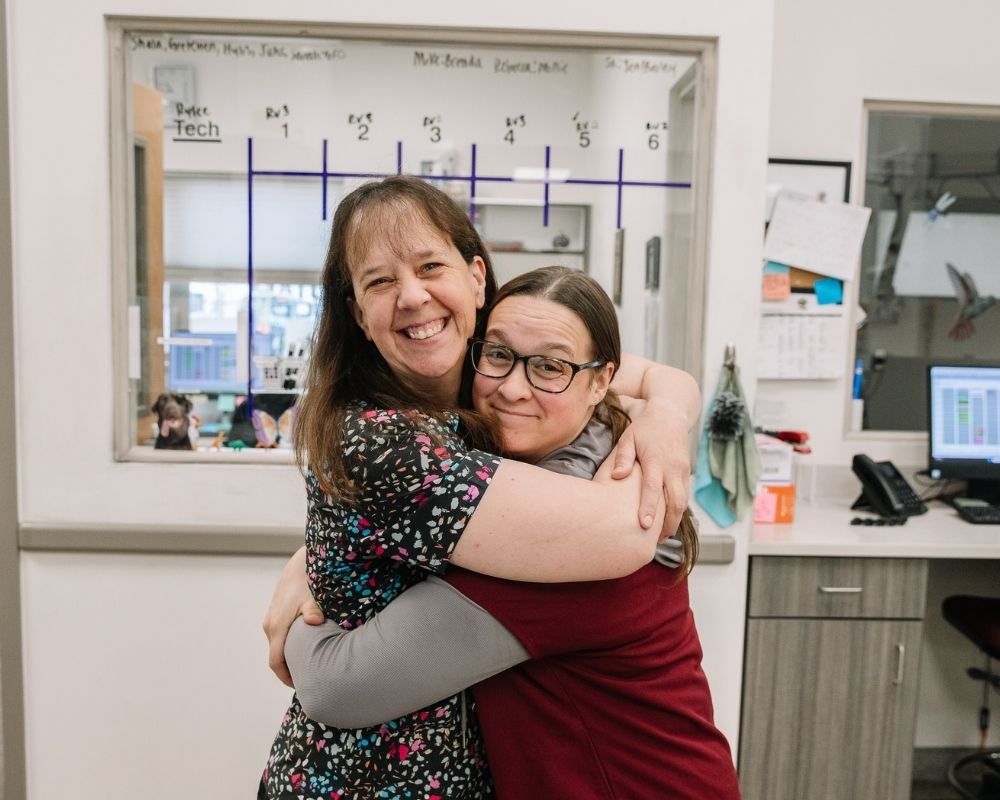 Two-people-embracing Two people embracing and smiling in what appears to be a medical or laboratory setting