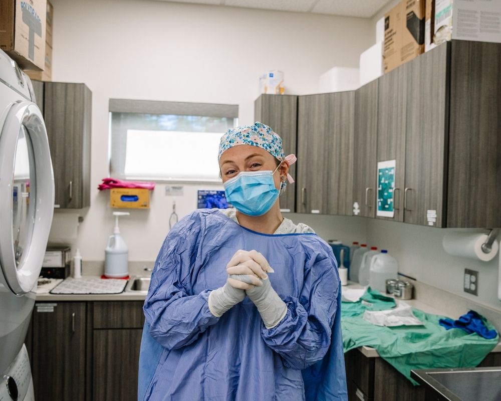 Image 2 Veterinary team member wearing a surgical gown, mask, and gloves, standing in a veterinary treatment room
