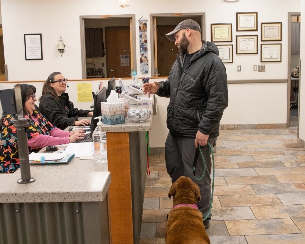 a-man-with-a-pet A man holding a leash stands with his dog at a veterinary clinic reception desk