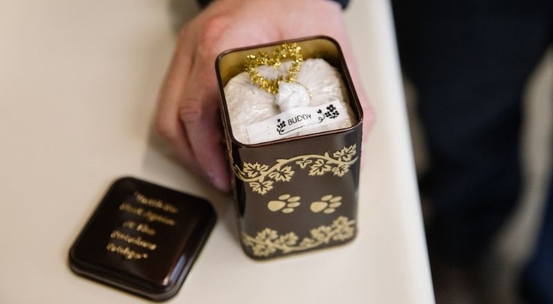 A small decorative tin with a lid next to it, containing a white fluffy object tied with a gold ribbon.