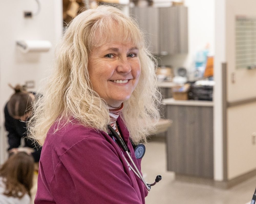 Image 2 A woman in a maroon scrub top and striped long sleeve shirt smiles at the camera